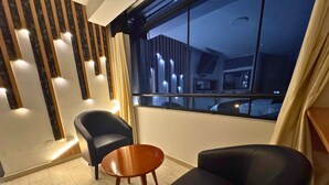 A modern room with two black leather chairs, a small wooden table, and a large window with a view of the outside. - City Tower Hotel (Santiago de Surco)
