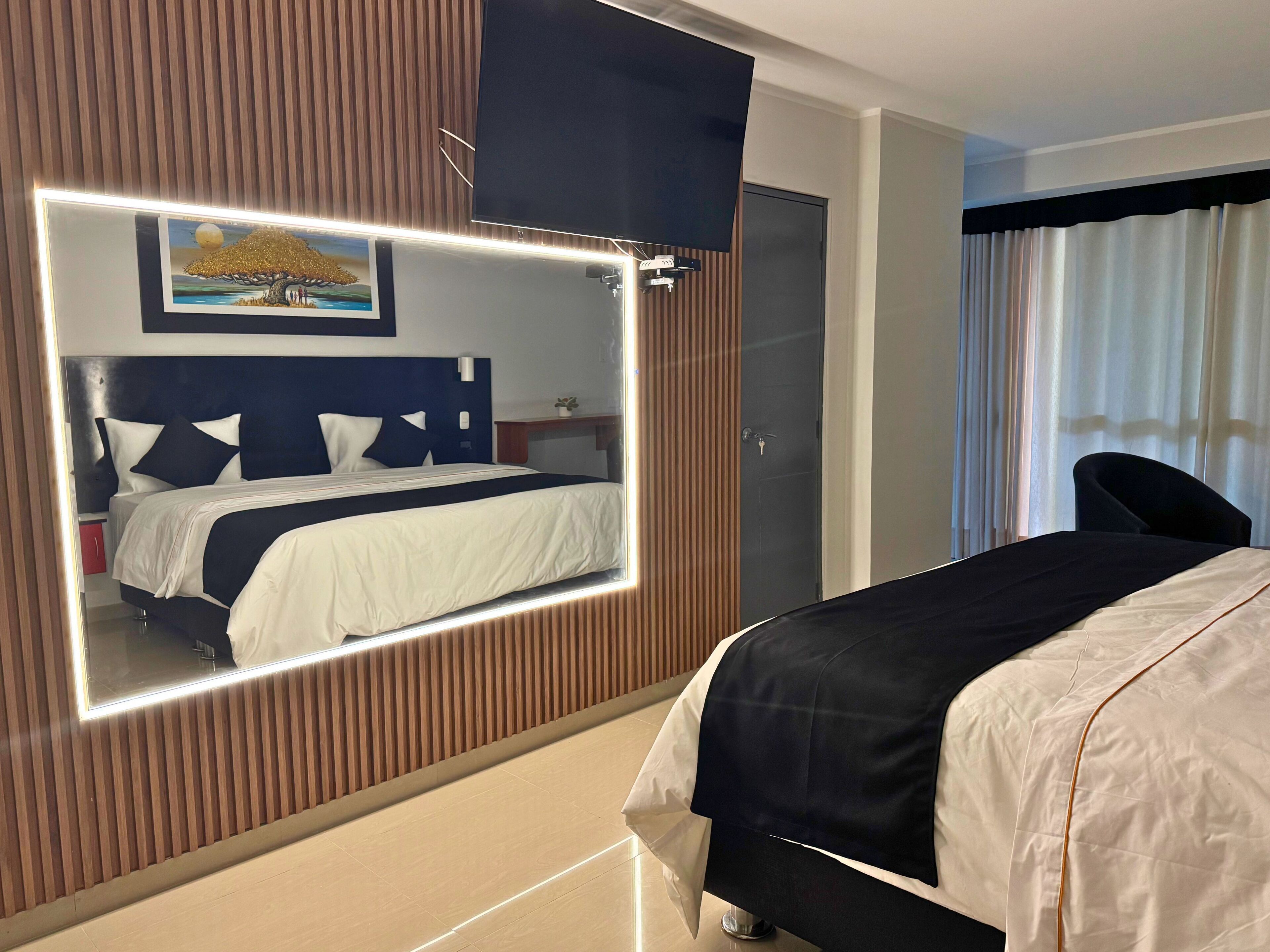 Una habitación de hotel con cama, mesita de noche, espejo y un cuadro en la pared.
