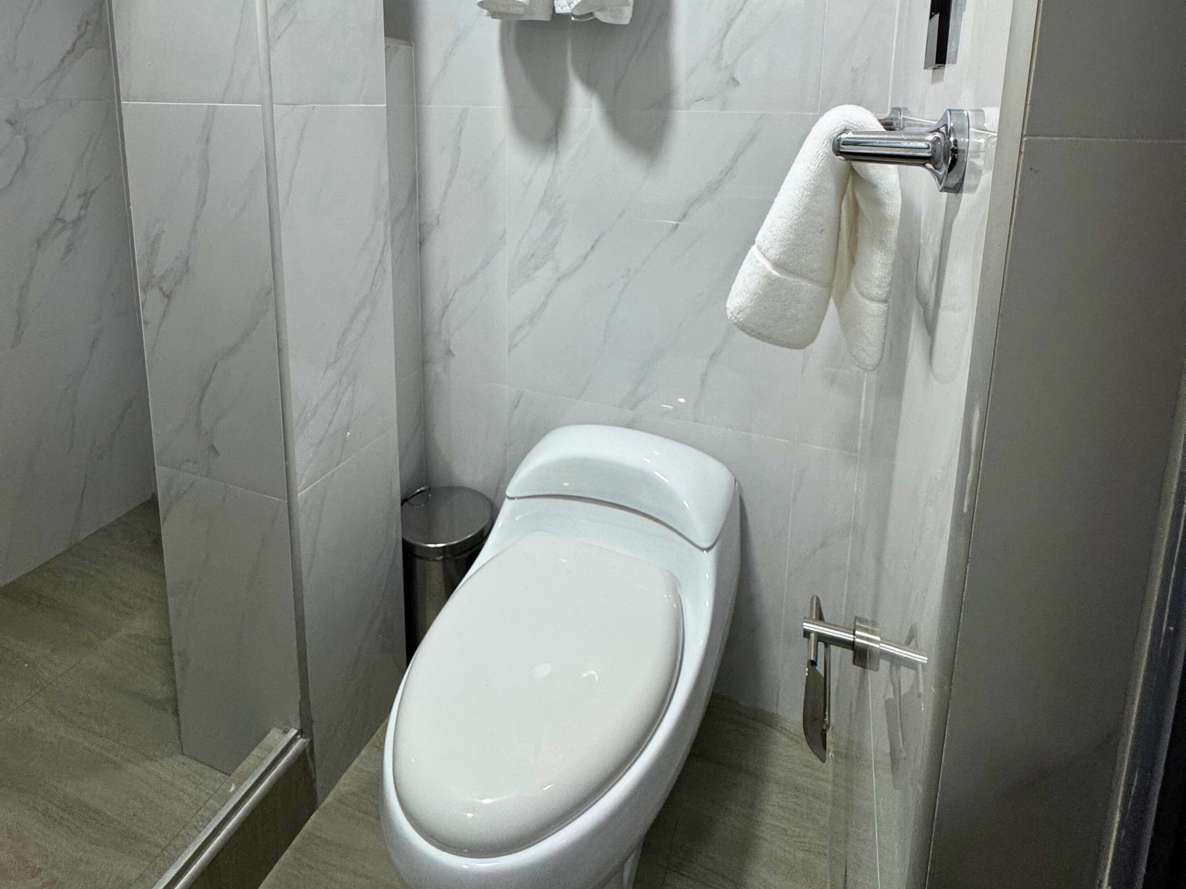 Un baño moderno con un inodoro blanco, un cubo de basura y un perchero para toallas.