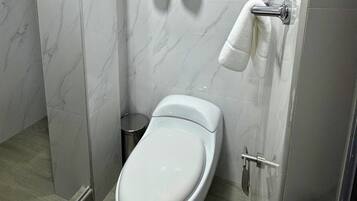 Un baño moderno con un inodoro blanco, un cubo de basura y un perchero para toallas.