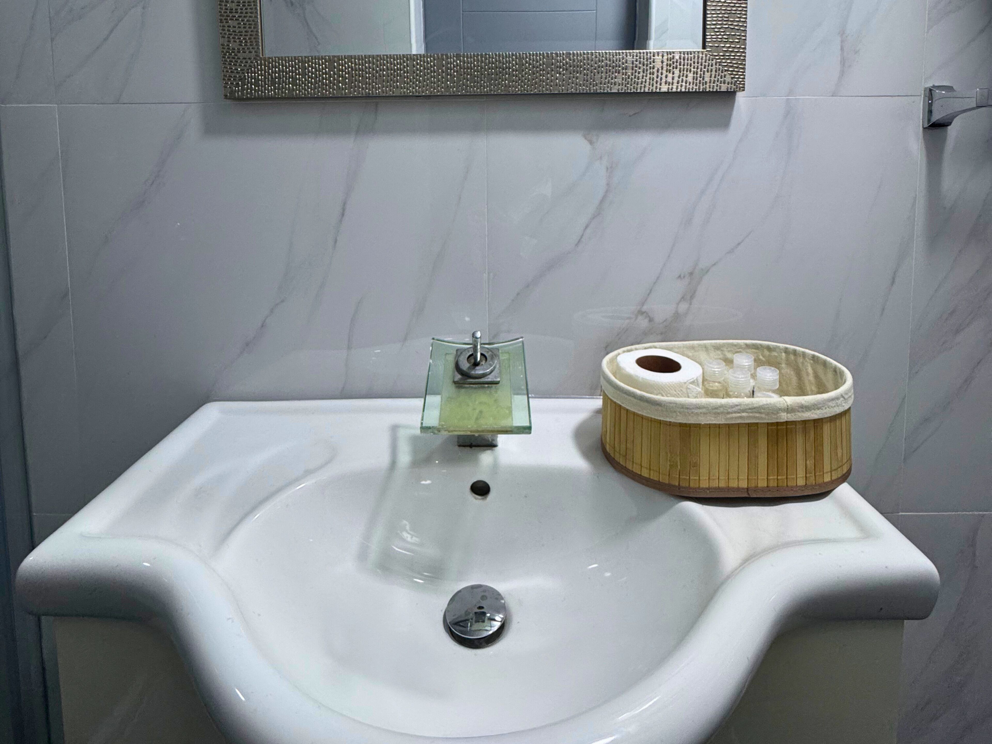 Ein Badezimmer mit einem weißen Waschbecken, einem Spiegel darüber und einem Holzkorb mit Pflegeprodukten.