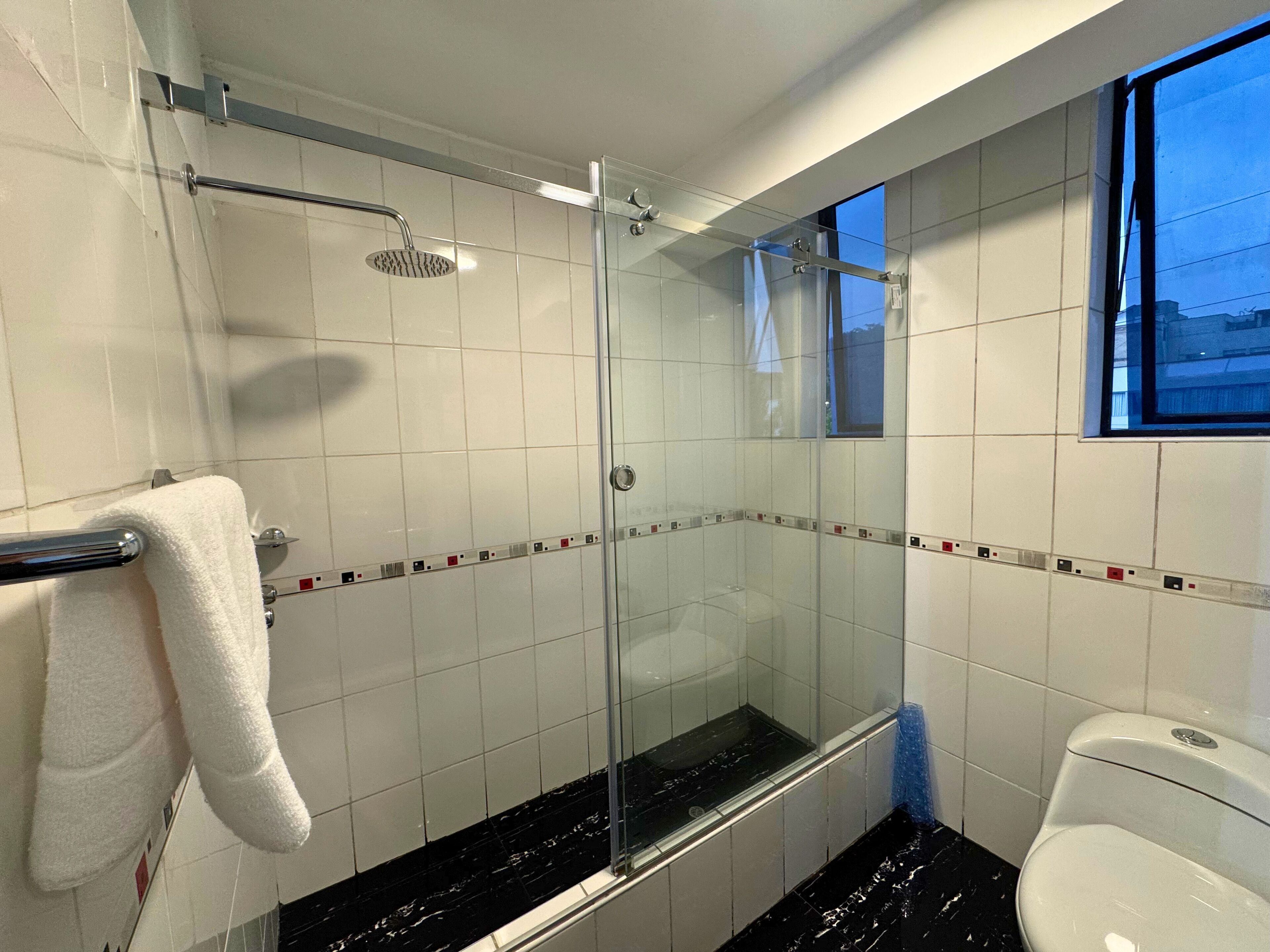 Un baño moderno con cabina de ducha de vidrio, un inodoro blanco y un ventanal que ofrece luz natural.