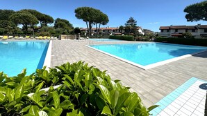 Una piscina con due aree separate, circondata da un solarium in legno e sedie a sdraio gialle.
