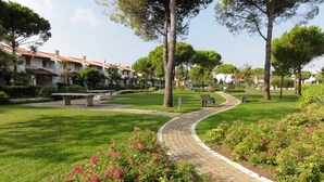 Un sentiero che si snoda in un parco, con panchine, alberi e un parco giochi sullo sfondo.