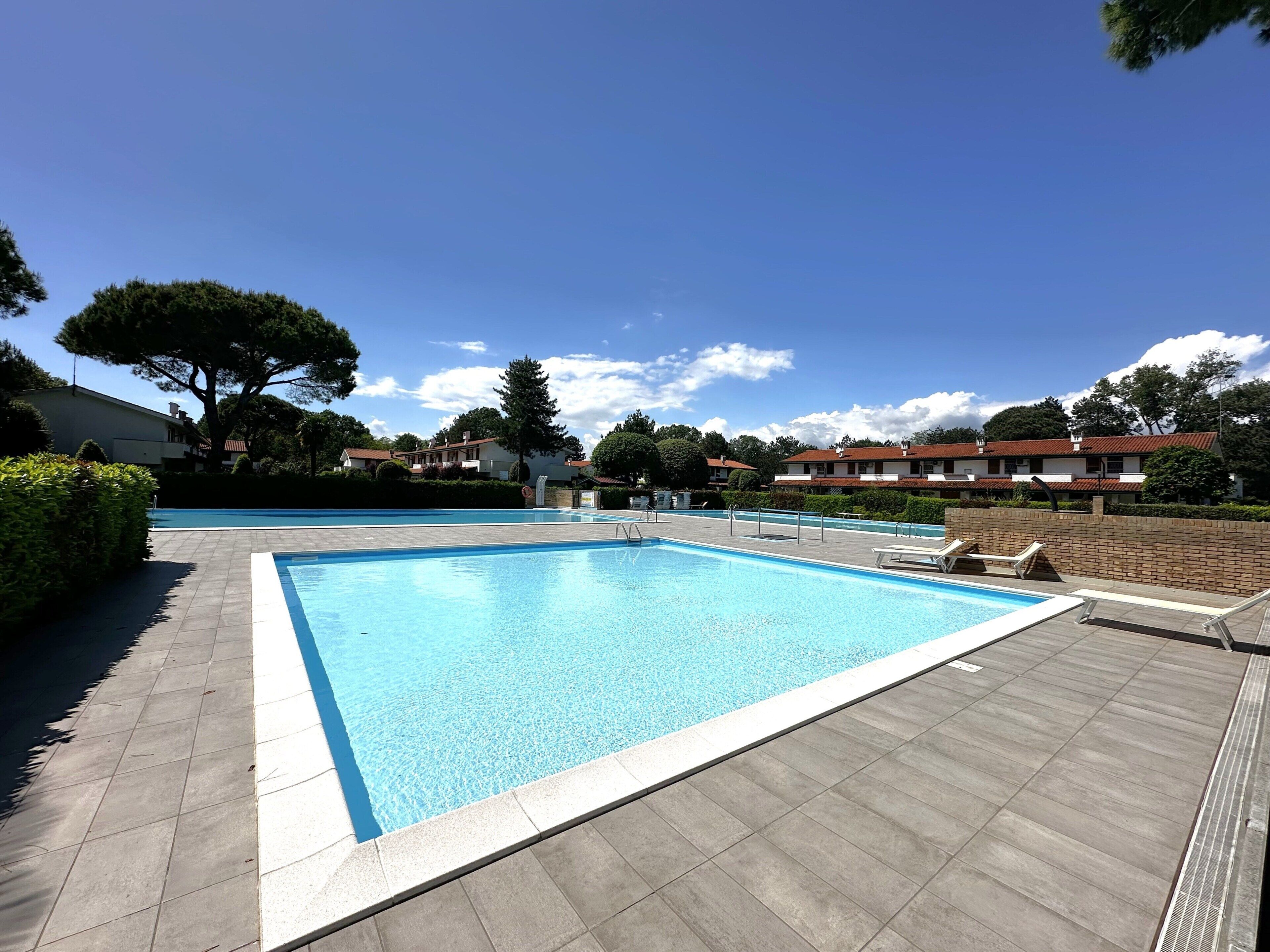 Una piscina rettangolare con bordo piastrellato, circondata da un basso muro in mattoni e un siepe.