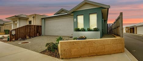 Einbungalow mit Garage, ein Vorgarten mit Blumenbeet und Blick auf die Straße.