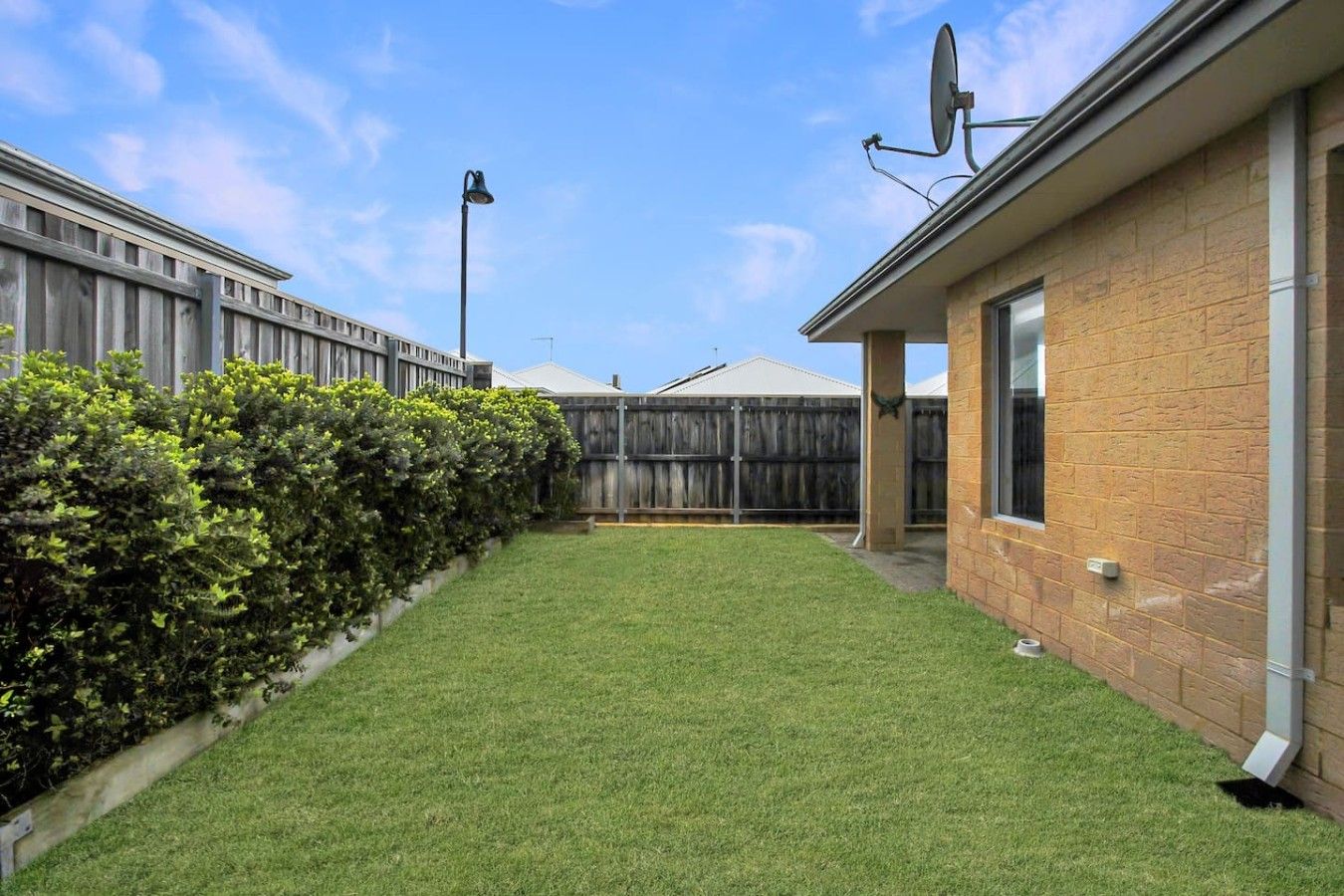 A backyard with a well-maintained lawn, a wooden fence, and a brick building with a satellite dish.