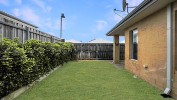 A backyard with a well-maintained lawn, a wooden fence, and a brick building with a satellite dish.