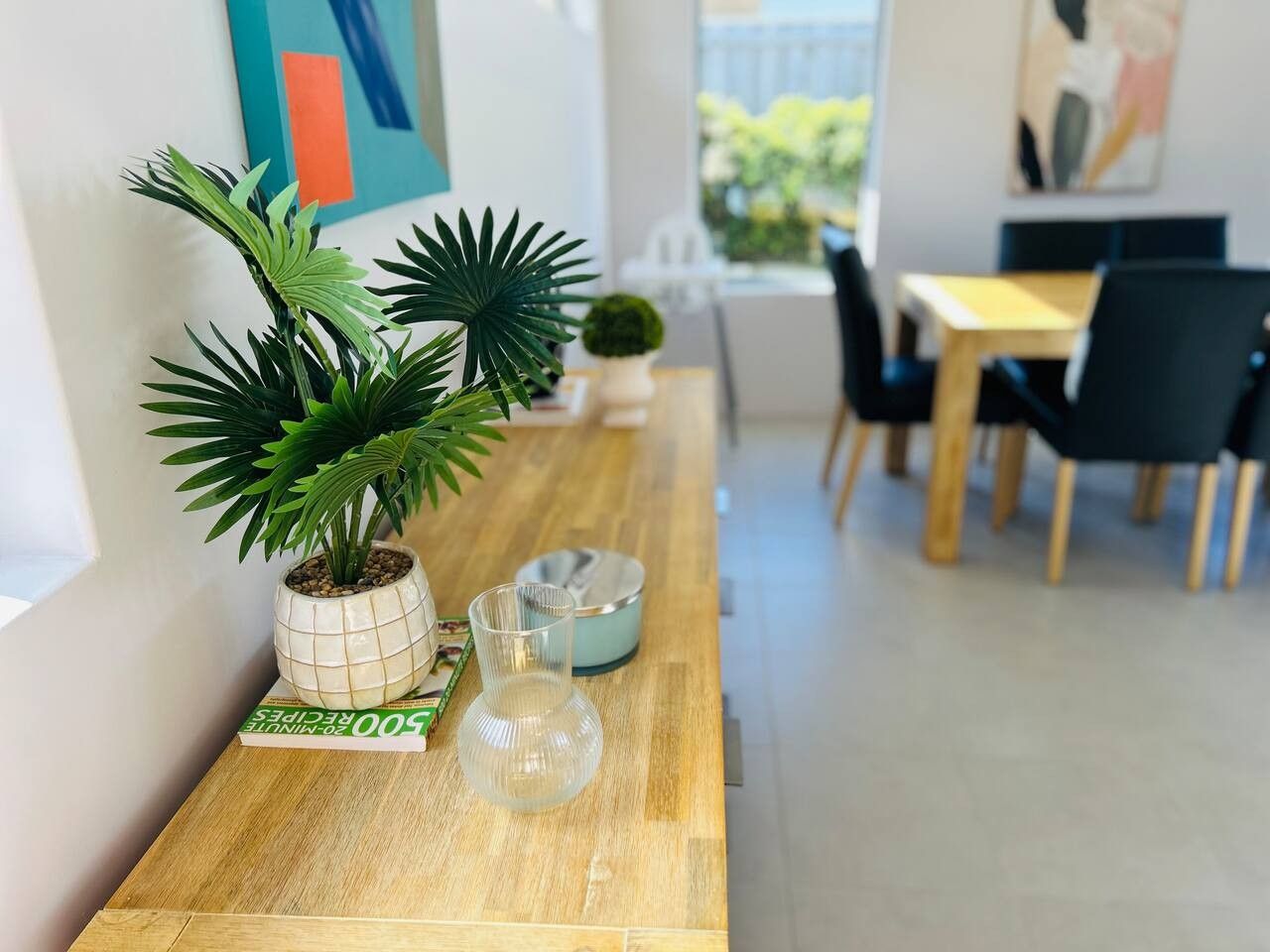 A wooden table with a potted plant, a glass vase, and a book.