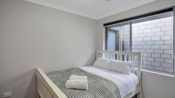A bedroom with a single bed, a window with blinds, and a white ceiling vent.
