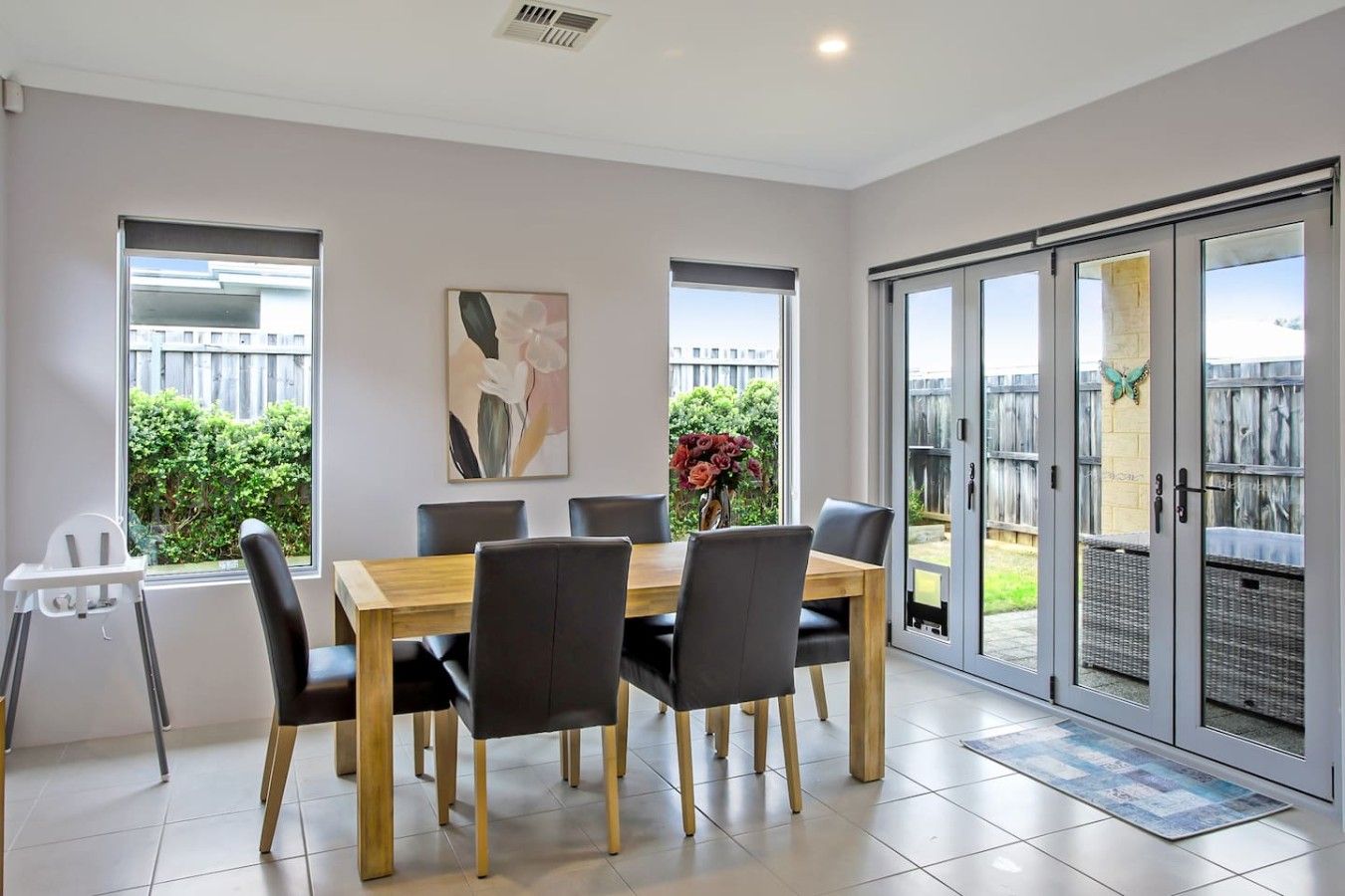 A dining area with a table and chairs, a window with a view of greenery, and a sliding glass door leading to an outdoor space.