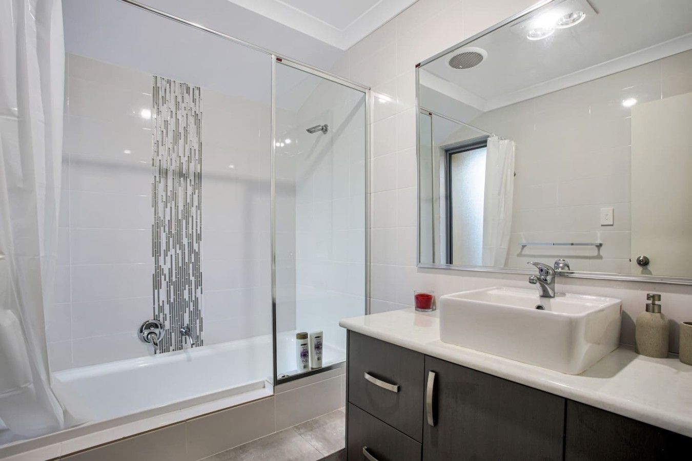 A modern bathroom with a glass shower enclosure, a white sink, and a large mirror.