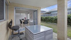Un patio couvert comprenant une table et des chaises, un barbecue et un pouf en osier.