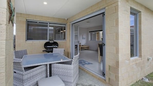 Un espace extérieur aménagé en patio, avec une table et des chaises, un barbecue et une porte-fenêtre coulissante donnant sur l’intérieur.