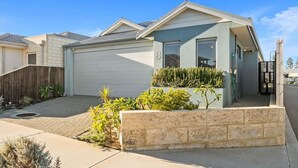Une maison d’habitation avec un garage, un jardin devant la maison agrémenté de plantes et un ciel dégagé.