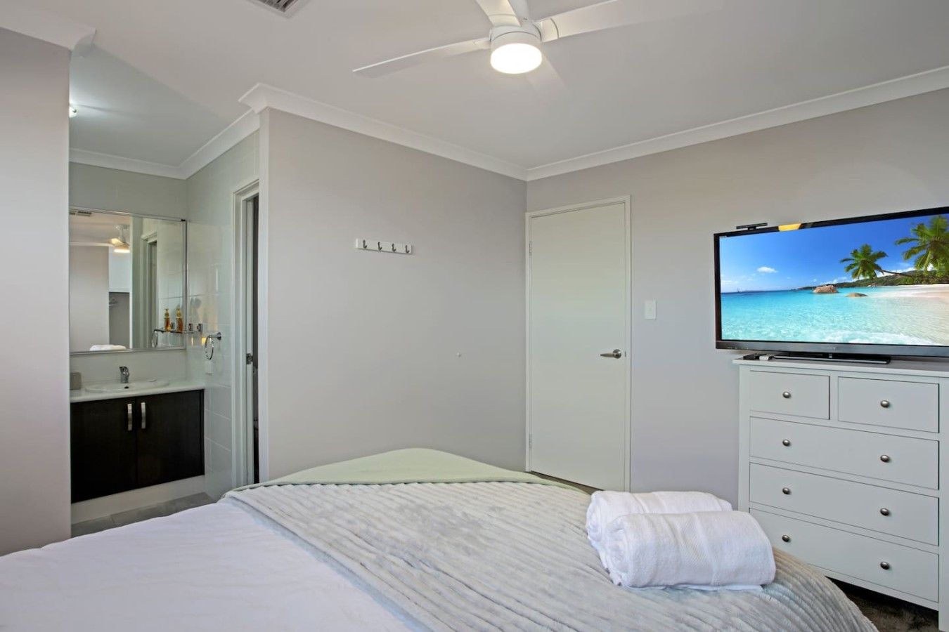 A bedroom with a bed, a television on a dresser, a bathroom with a mirror, and a door.