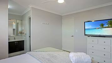 A bedroom with a bed, a television on a dresser, a bathroom with a mirror, and a door.