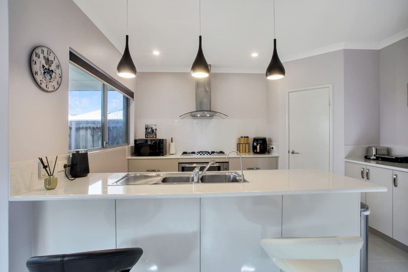 A modern kitchen with a central island, pendant lighting, and a view through the window.