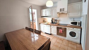 Une cuisine compacte avec des meubles blancs, une table à manger en bois, un lave-linge et un four à micro-ondes.