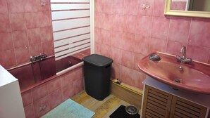 Une salle de bain avec des carreaux roses, une baignoire, un lavabo et un miroir.