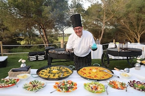 A chef preparing food outdoors with large pans of dishes, a grill, and various salads and vegetables on tables. - villa salvaje beach (PALMA DE MALLORCA)