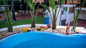 Een zwembadterras met een tafel gedekt met eten en drinken, omringd door planten en een waterpartij.