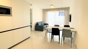A modern kitchen with a built-in microwave, a dining area with a table and chairs, and a living area with a sofa and a TV. - Apartment in a Prime Seafront Location (San Michele al Tagliamento)