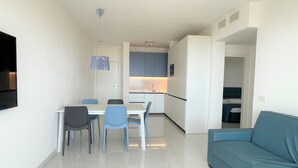A modern apartment with a dining area, kitchenette, and a living room with a sofa. - Apartment in a Prime Seafront Location (San Michele al Tagliamento)