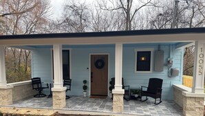 A covered porch with stone columns, a door with a wreath, and a number '1055' on the wall.