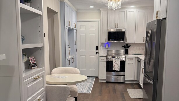 A modern kitchen with white cabinetry, stainless steel appliances, and a chandelier.
