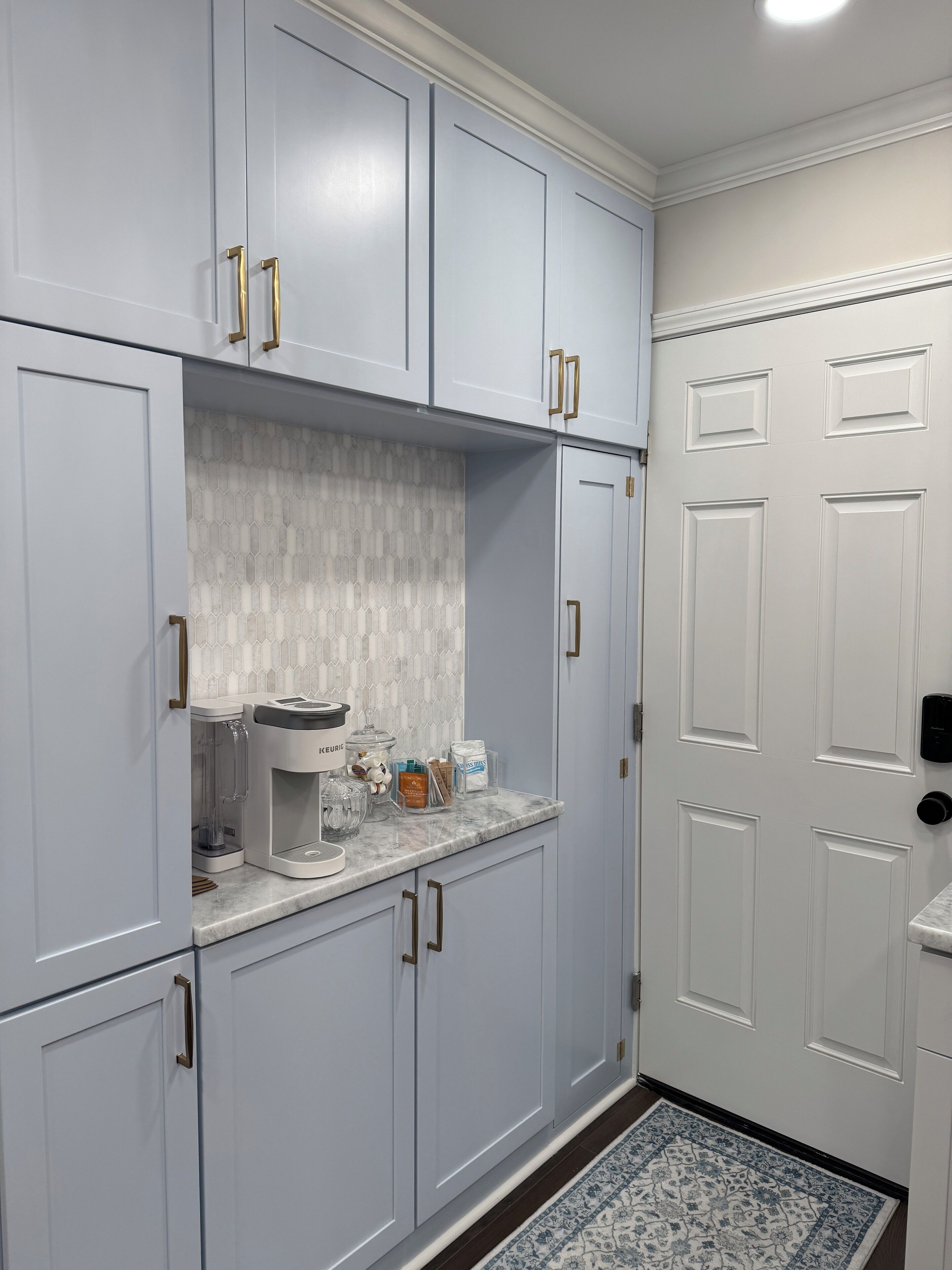 A kitchen with light blue cabinets, a coffee maker, and a door with a keypad lock.
