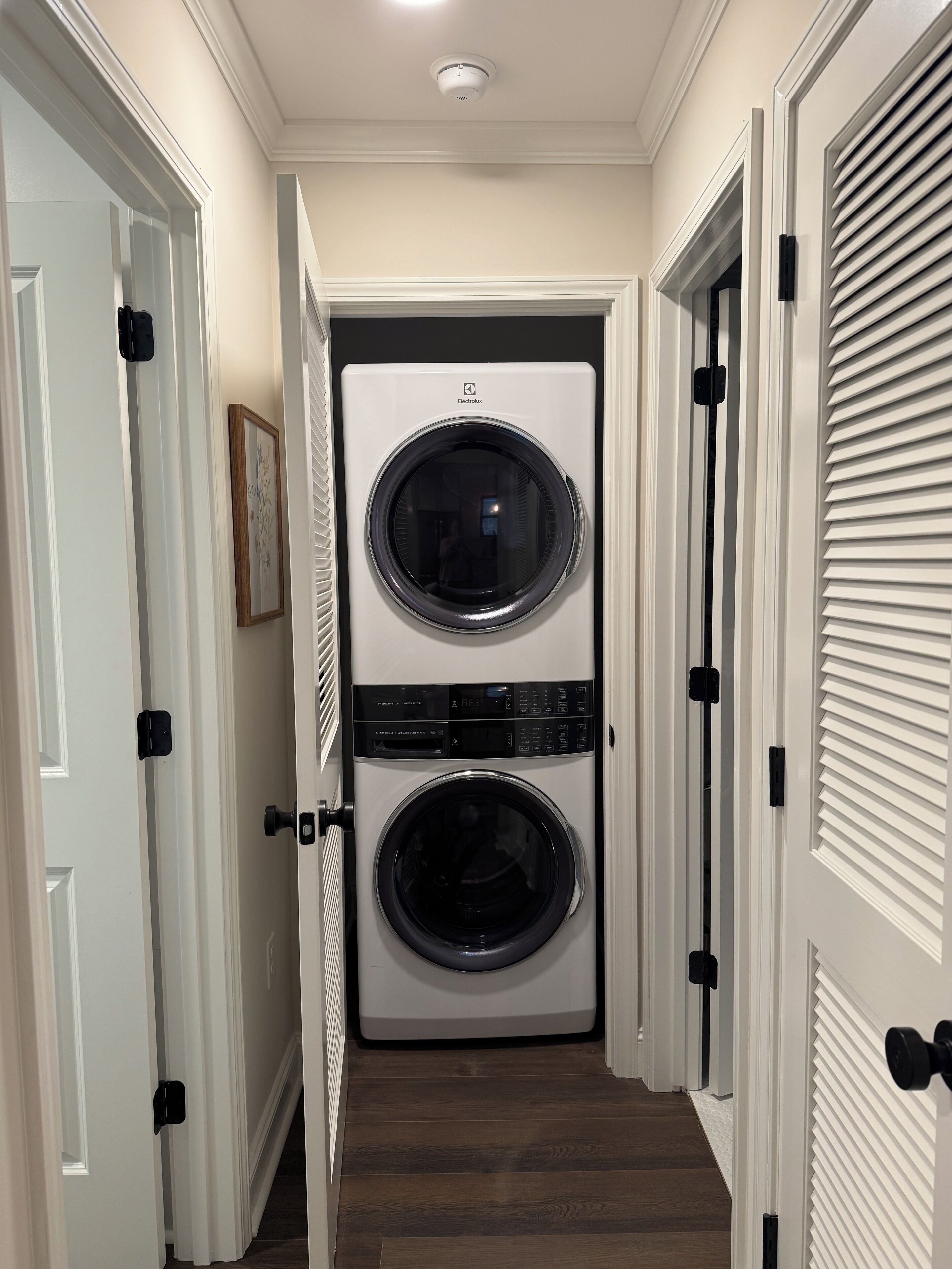 A laundry room with two stacked front-loading washing machines, a ceiling light, and a door with a black handle.