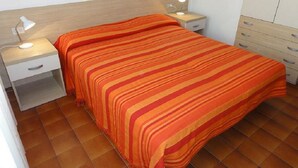 A bedroom with a bed, two bedside tables with lamps, a wardrobe, and a tiled floor. - Central Bibione Apartment With Terrace (San Michele al Tagliamento)