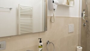 A bathroom with a hairdryer mounted on the wall, a towel rack, a bottle of olive oil, and a shower area. - AuGuStea-The Nest of Sannicandro (Bari)