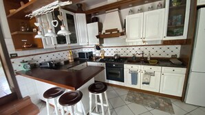A kitchen with white cabinets, a wooden countertop, a stove, a sink, and three stools. - The Lake House (Castel Gandolfo)