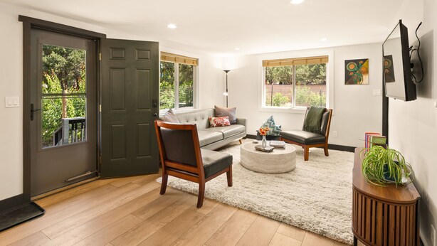 A living room with a grey sofa, wooden chairs, a round coffee table, and a small wooden side table with a plant. - The Green Gem (Crestone)