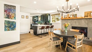 A modern kitchen with dark cabinets, a central island, and a dining area with a round table and chairs. - The Green Gem (Crestone)