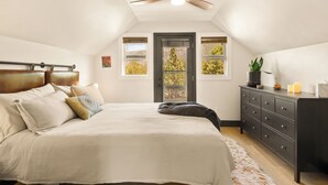 A bedroom with a bed, a dresser, a ceiling fan, a door, and windows. - The Green Gem (Crestone)