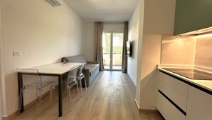 A modern kitchen with a built-in stove, a dining area with a table and chairs, and a sliding glass door leading to a balcony. - Modern Apartment in Central Bibione (San Michele al Tagliamento)