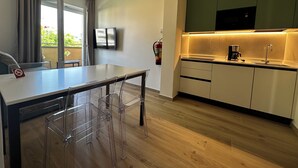 A modern kitchen with a dining area, wooden flooring, and a flat-screen TV mounted on the wall. - Modern Apartment in Central Bibione (San Michele al Tagliamento)