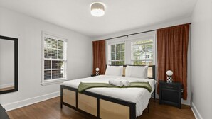 Une chambre à coucher avec un lit, deux fenêtres équipées de stores, un radiateur et un luminaire au plafond.
