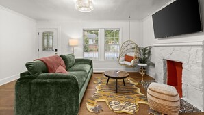 Un salon avec un canapé vert, une table basse ronde, un fauteuil suspendu, une cheminée et un téléviseur fixé au mur.