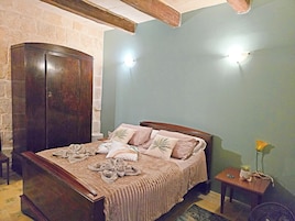 A bedroom with a wooden bed, a wardrobe, a bedside table with a plant, and a wall-mounted light fixture.