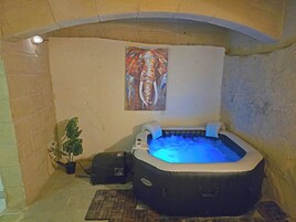 A hot tub with a blue light, a painting on the wall, and a potted plant.