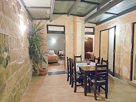 A narrow hallway with a dining area featuring a table and chairs, a bed in the background, and a potted plant.