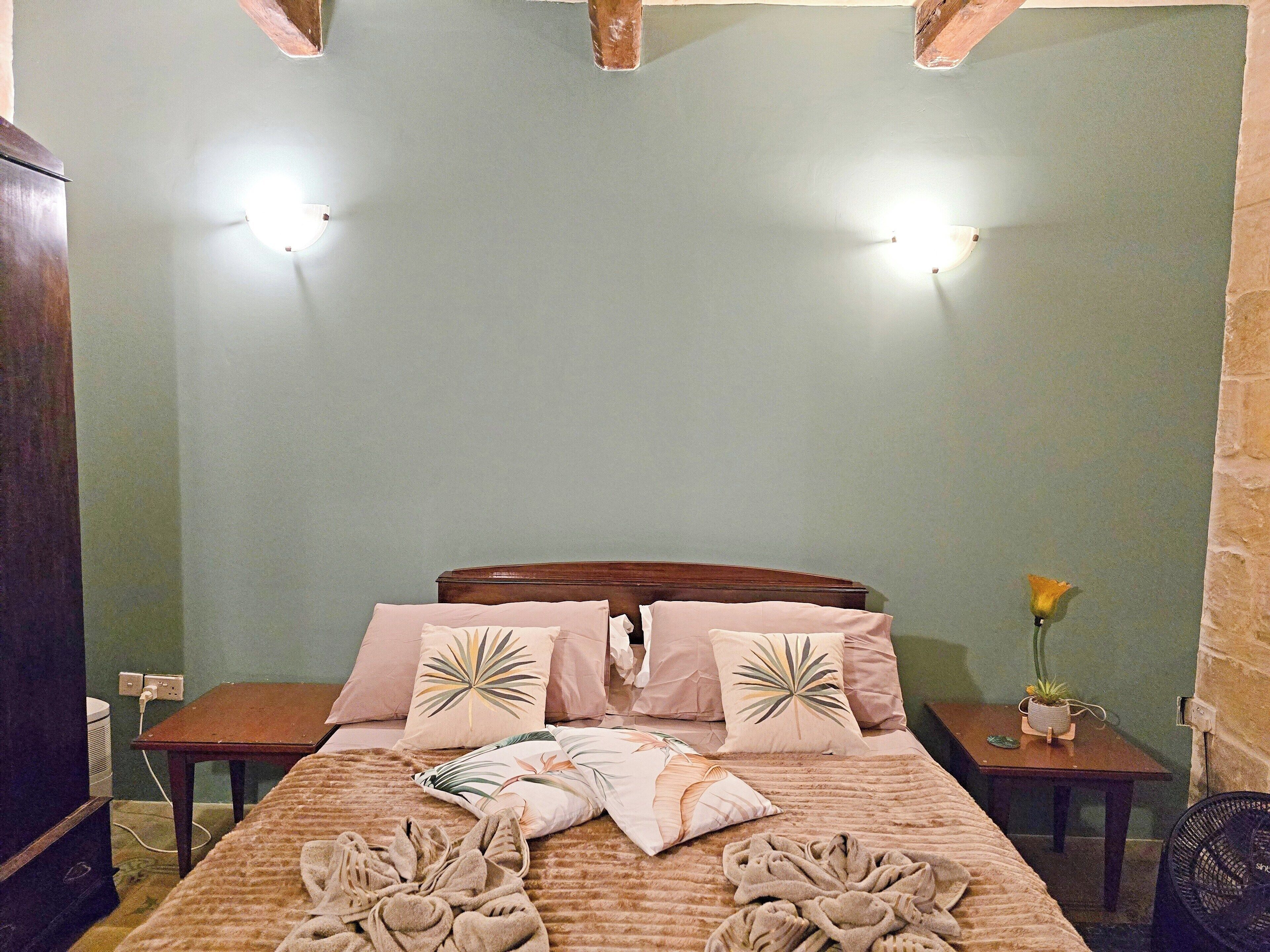 A neatly made bed with a patterned bedspread, two bedside tables with lamps, and a potted plant on one of the tables.