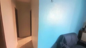 A narrow hallway leading to a room with a blue wall and a dark-colored sofa. - Apartamento em Belém no período da COP 30 (Belem)