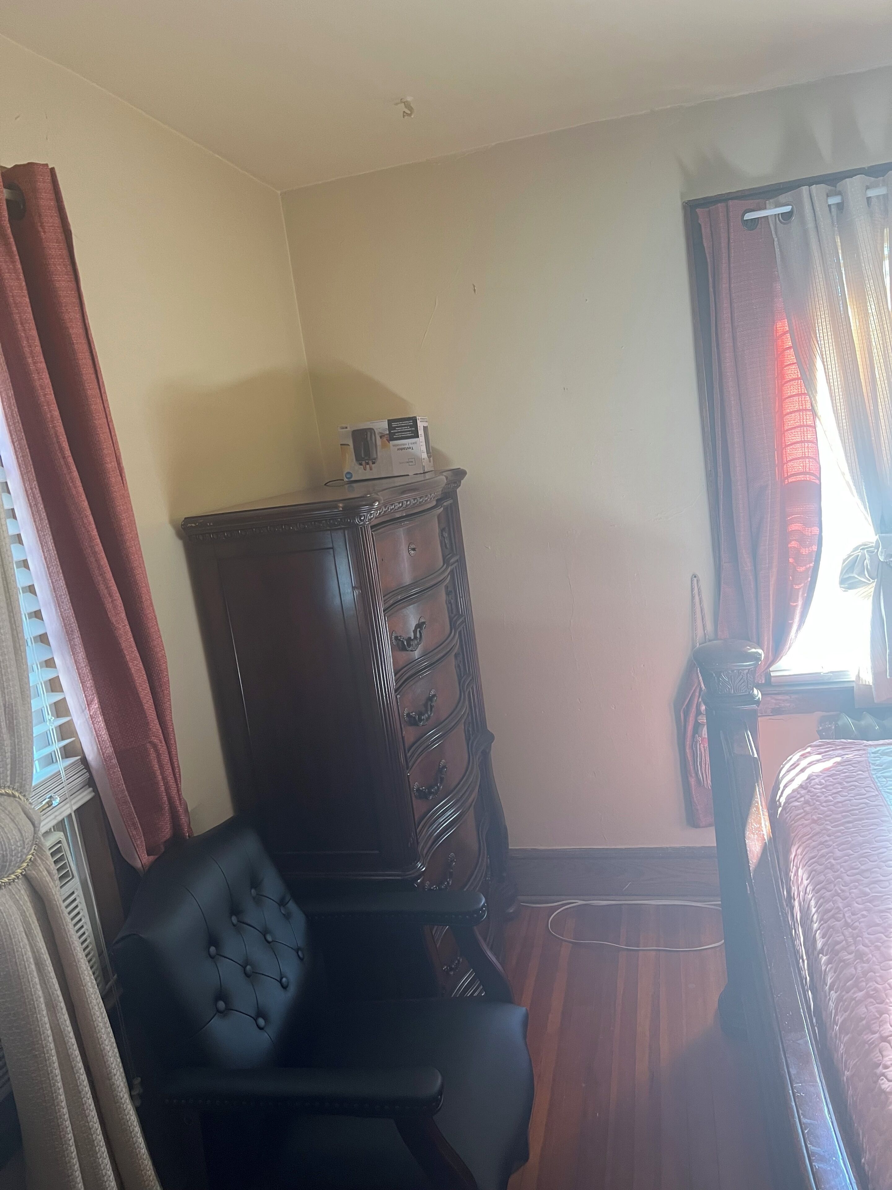 A room with a wooden dresser, a tufted chair, and a bed with a quilt.