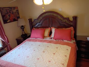 Ein Bett mit einer Blumensteppdecke, einem Holz-Kopfteil und zwei roten Kissen.