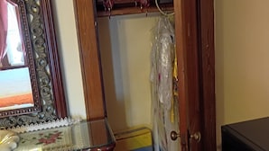 Une pièce comprenant une commode en bois, un miroir, une porte donnant sur un placard avec des étagères, et une boîte contenant des produits de la marque Oster.
